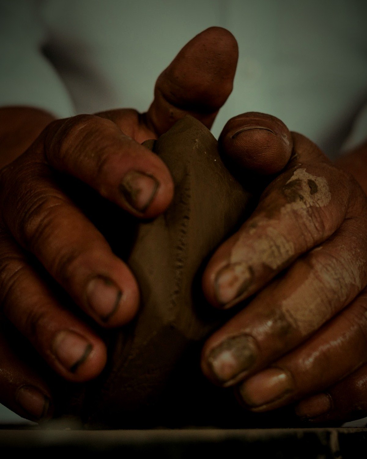 Two hands raising the wall of a vessel from the base, no wheel